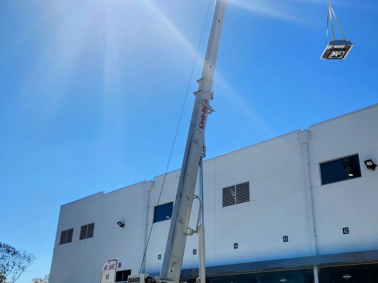 Bass Crane Link-Belt boom lifting a rooftop HVAC unit onto a commercial building