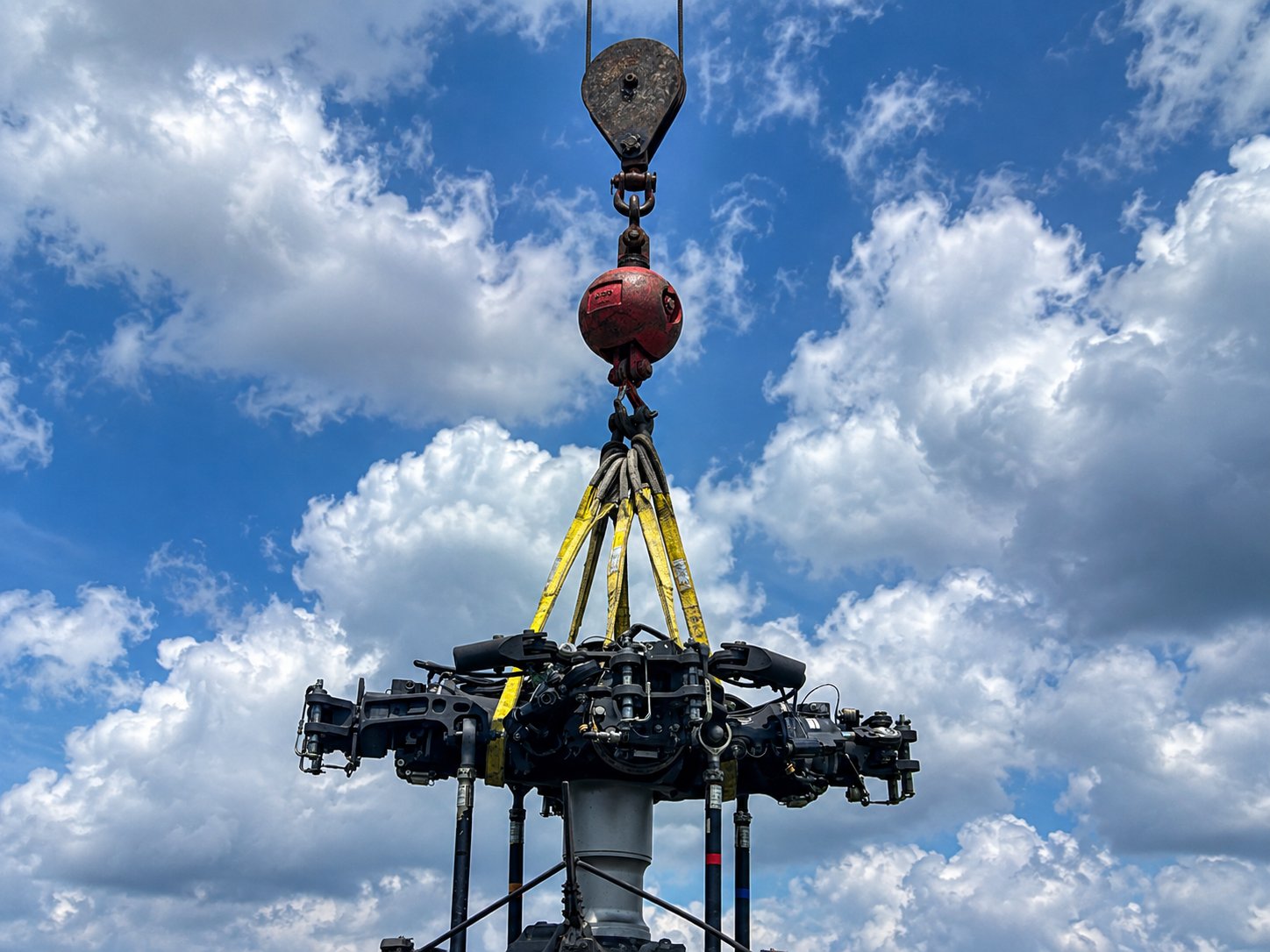 Crane hook block and yellow rigging slings attached to a helicopter rotor head